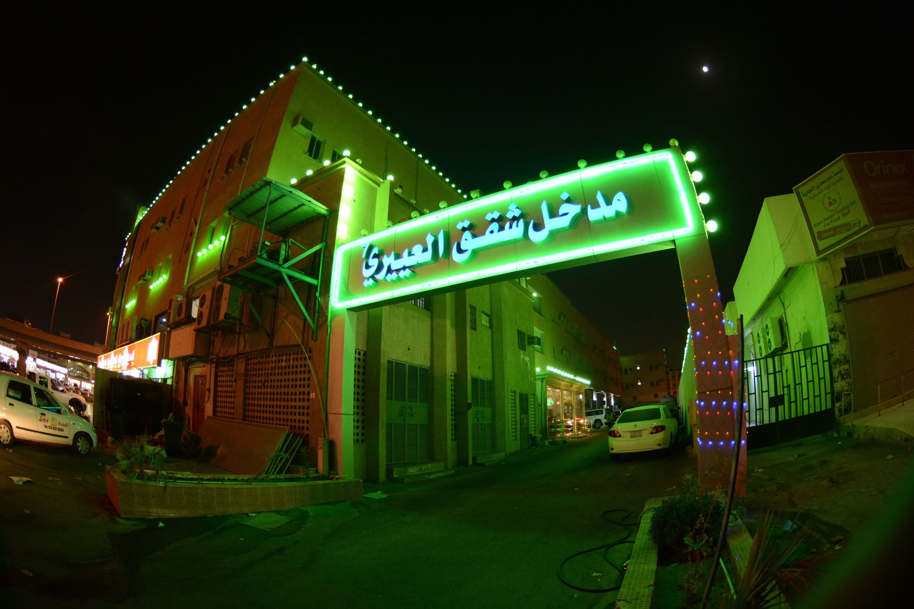 A building with a neon sign in Arabic, a gated entrance, and a parked car in front.