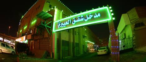A building with a neon sign in Arabic, a gated entrance, and a parked car in front.