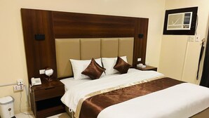 Una habitación de hotel con una cama grande, cabecera de madera, mesita de noche con lámpara, un cesto de basura y un aire acondicionado de pared.