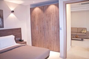 Een moderne slaapkamer met een groot bed, een houten garderobe en een bankje in de aangrenzende woonkamer.