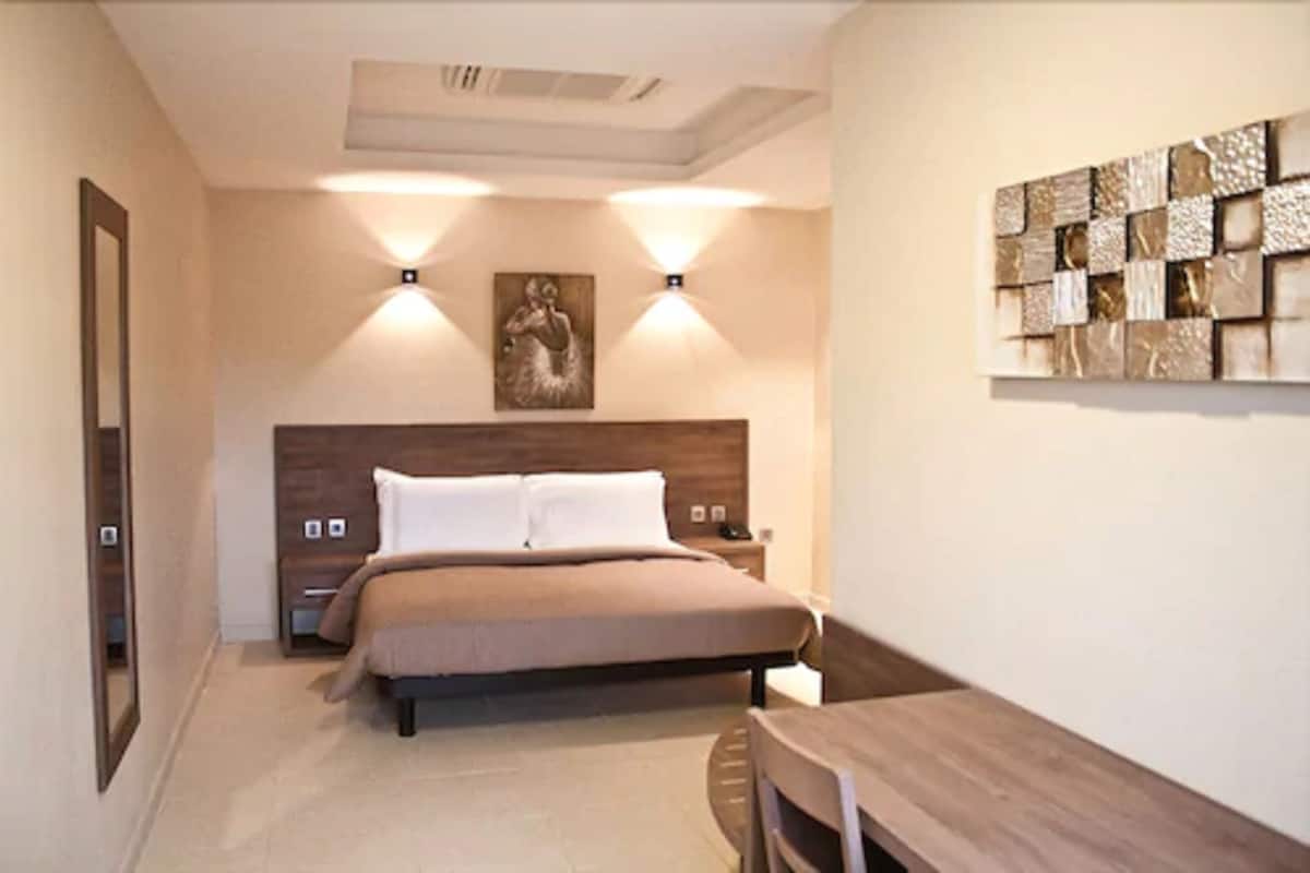 A bedroom with a bed, bedside tables, a nightstand, a wall-mounted artwork, and a decorative wall panel.
