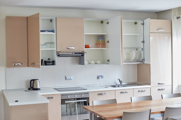 A modern kitchen with open cabinets, a built-in oven, and a dining area with a wooden table and chairs.