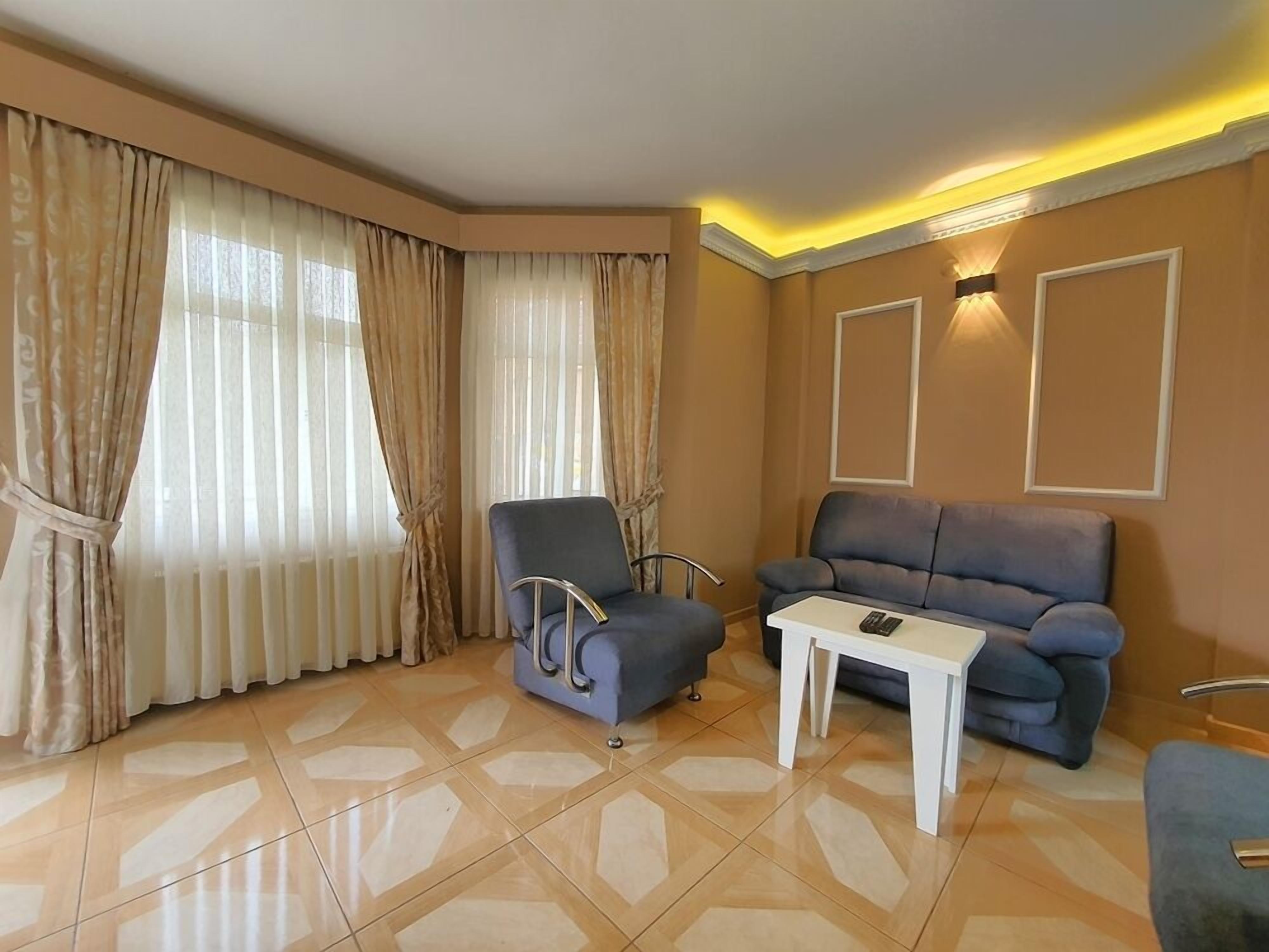 A hotel room with a blue armchair, a sofa, a small white table, and a lamp on the wall.
