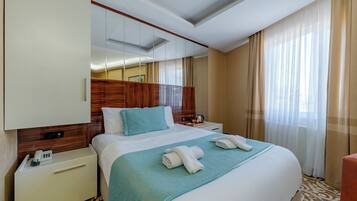 A hotel room with a large bed, a bedside table with a phone, a mirror, and a window with curtains.