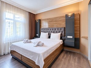 Habitación de hotel moderna con una cama grande, cabecero de madera y vista a la ciudad por la ventana.