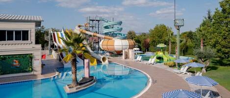 A swimming pool with a water slide, lounge chairs, and umbrellas.