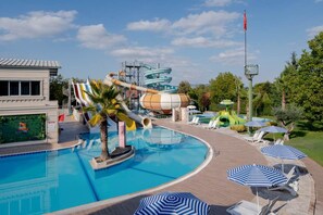 Ein Schwimmbecken mit Wasserrutsche, Liegestühlen und Sonnenschirmen.