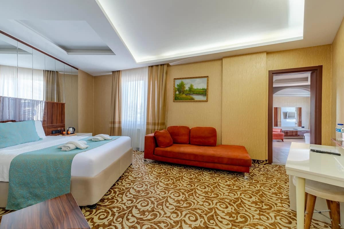 A hotel room with a bed, a sofa, a desk, and a painting on the wall.