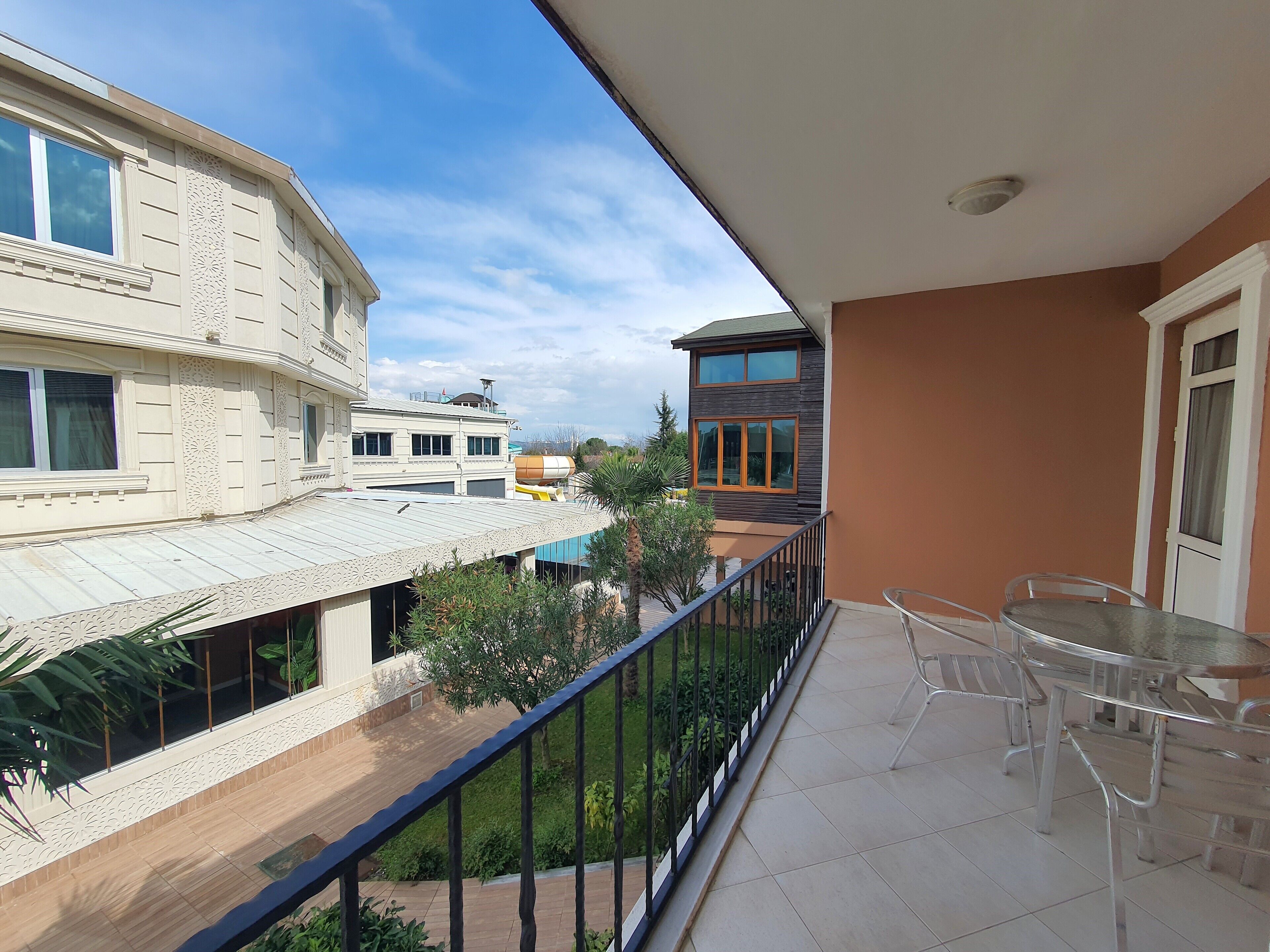 Un balcón con una mesa y sillas, que da a un patio con edificios y vegetación.