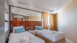 Ein Hotelzimmer mit zwei Betten, einem großen Spiegel, einem Holz-Kopfteil, einem Nachttisch und einem Fenster mit Vorhängen.