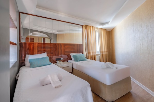 Habitación de hotel con dos camas, un espejo grande, cabecera de madera, mesita de noche y ventana con cortinas.