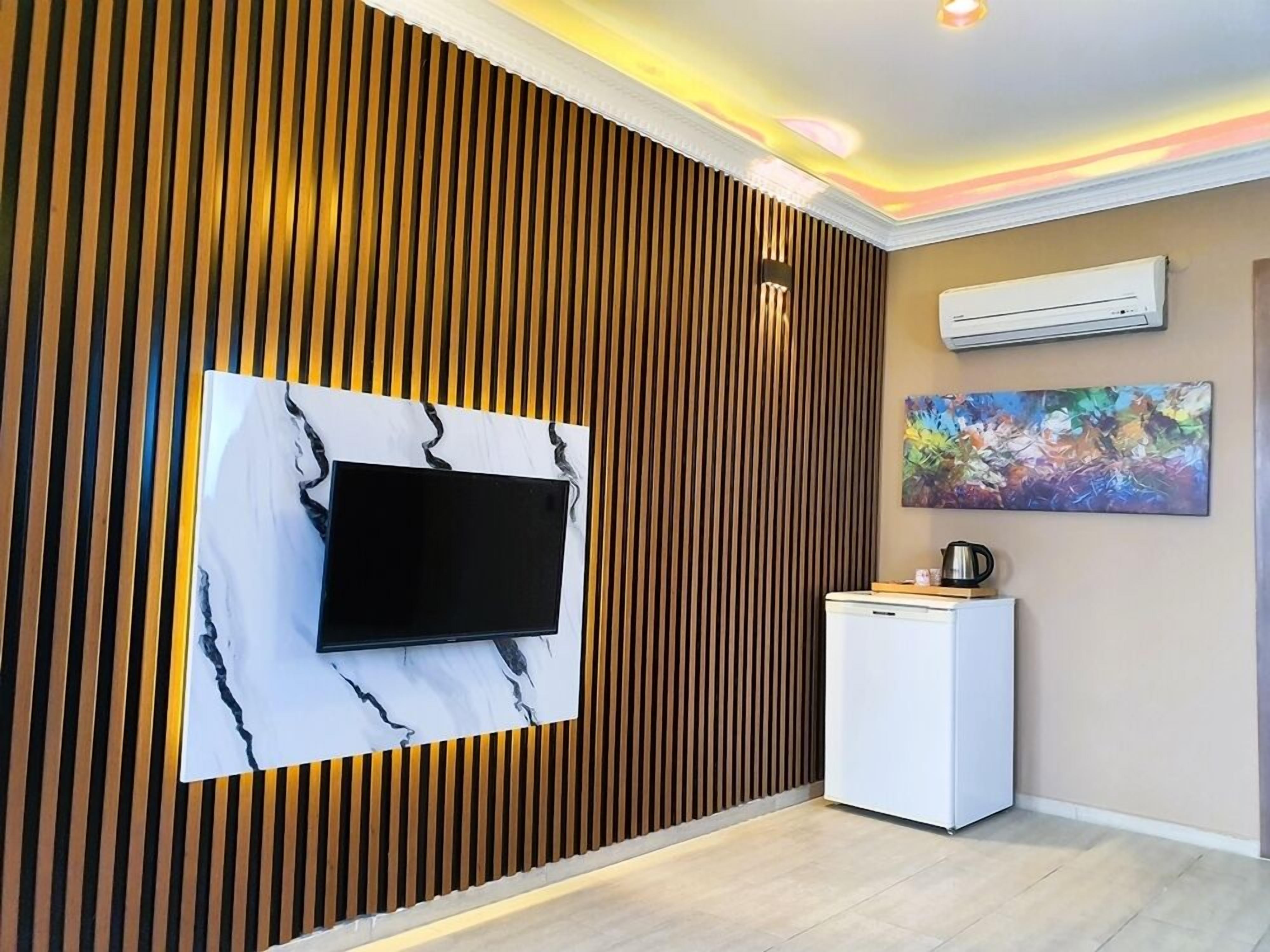 Una habitación moderna con un muro de listones de madera, un televisor de pantalla plana montado sobre una superficie similar al mármol, un pequeño armario blanco y un equipo de aire acondicionado en la pared.