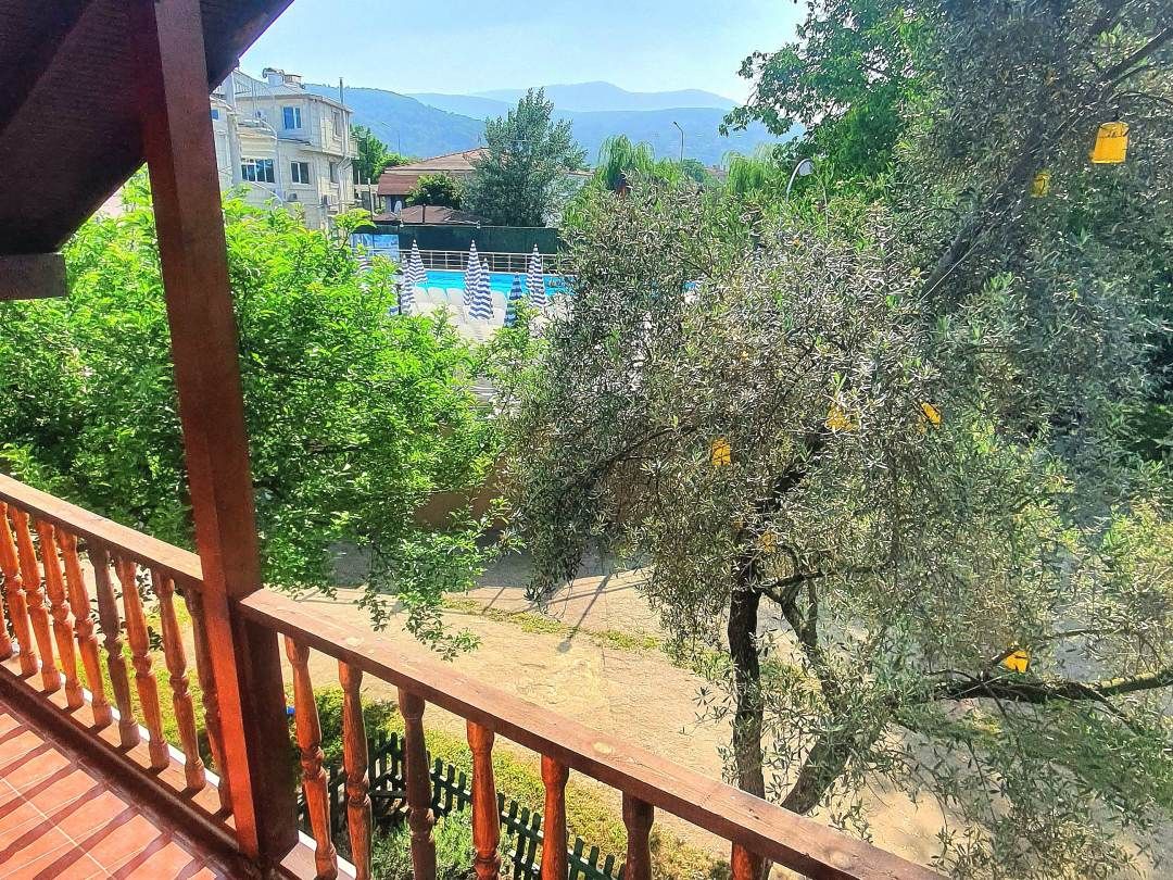A balcony with a view of a swimming pool, trees, and distant buildings.