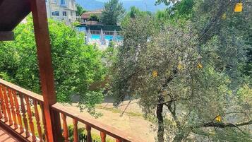 A balcony with a view of a swimming pool, trees, and distant buildings.