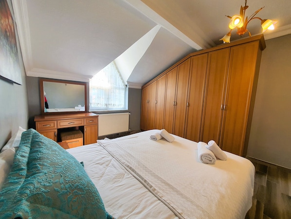 Un dormitorio con una cama, un armario de madera, un escritorio, un espejo y una ventana con cortinas.