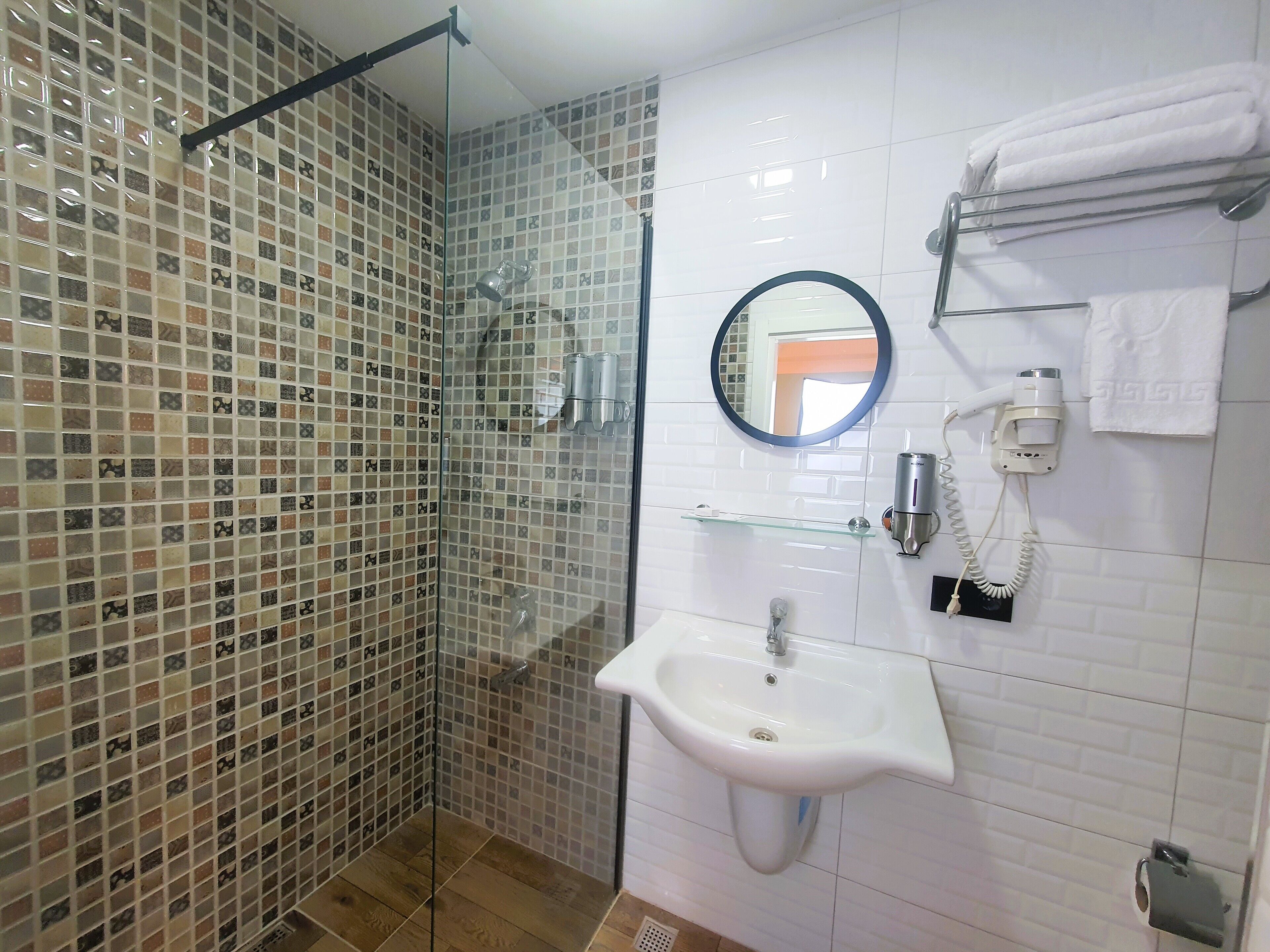 Een badkamer met een douchecabine van glas, een wastafel, een spiegel en een handdoekhouder.
