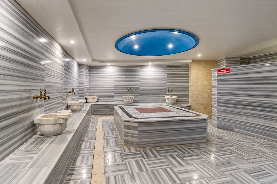 A modern bathroom with marble walls, a central sink area, and a blue ceiling light.