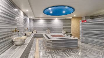 A modern bathroom with marble walls, a central sink area, and a blue ceiling light.