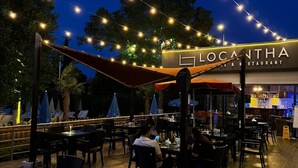 Ein Essbereich im Freien mit Lichterketten, Tischen und Sonnenschirmen vor dem Restaurant Locantha.