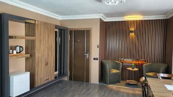 Ein modernes Zimmer mit dunklem Holzboden, einem Holzschrank, einem kleinen weißen Kühlschrank, einem Esstisch mit Stühlen und einem Wandheizkörper.