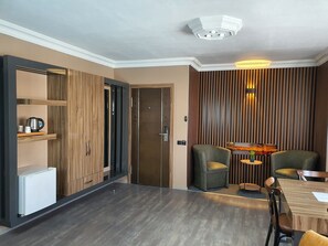 Une chambre moderne avec un plancher en bois foncé, une armoire en bois, un petit réfrigérateur blanc, une table à manger avec des chaises et un radiateur fixé au mur.