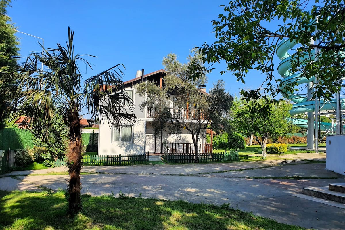 A modern two-story house with a white facade, surrounded by a well-maintained lawn and a black metal fence.