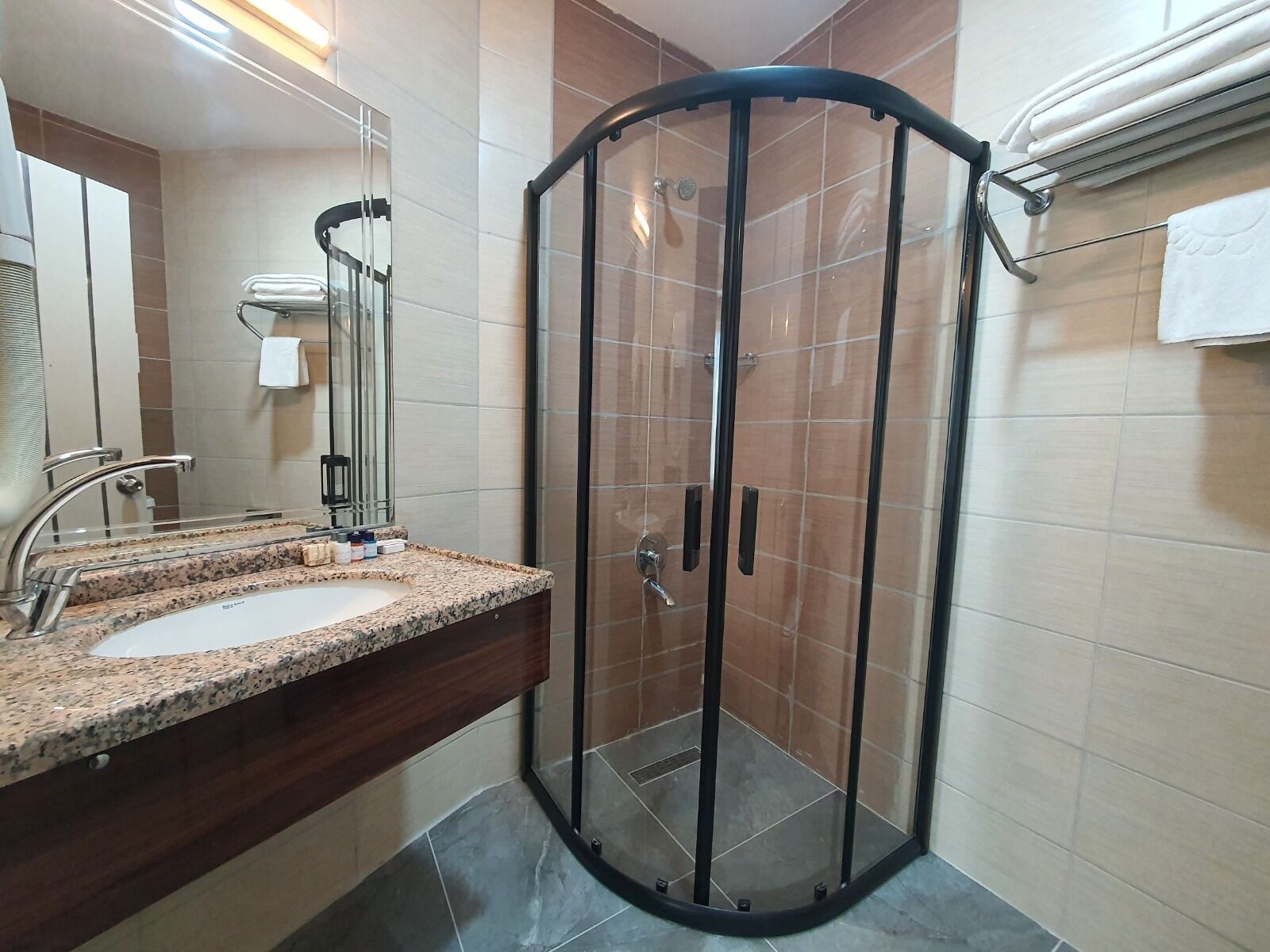 A modern bathroom with a glass-enclosed shower, a granite countertop sink, and a mirror.