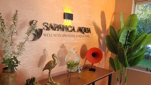 Ein Empfangsbereich mit einer Wandtafel mit der Aufschrift "Sapança Aqua Wellness Spa Hotel & Aqua Park", einer dekorativen Vogelplastik, einem Glasgefäß mit Grünpflanzen und einem Blumentopf.