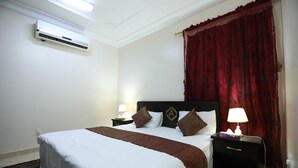 Une chambre d’hôtel avec un lit, une table de chevet, un climatiseur et un rideau rouge.