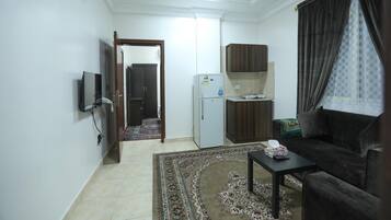 A compact living space with a kitchenette, a sofa, a coffee table, and a patterned rug.