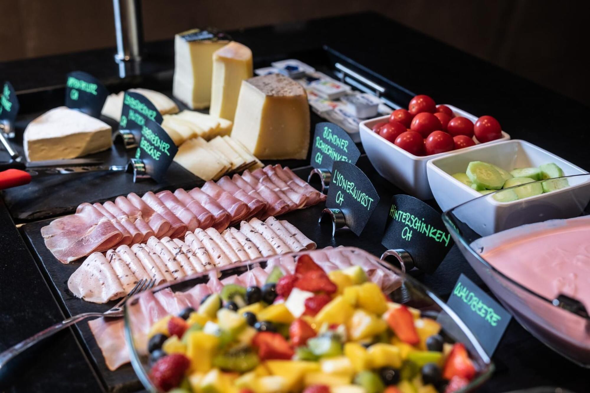 A buffet with various cheeses, cured meats, and fresh fruits.