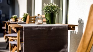 Een rij houten tafels met groene planten in potten en een glazen potje op elk.