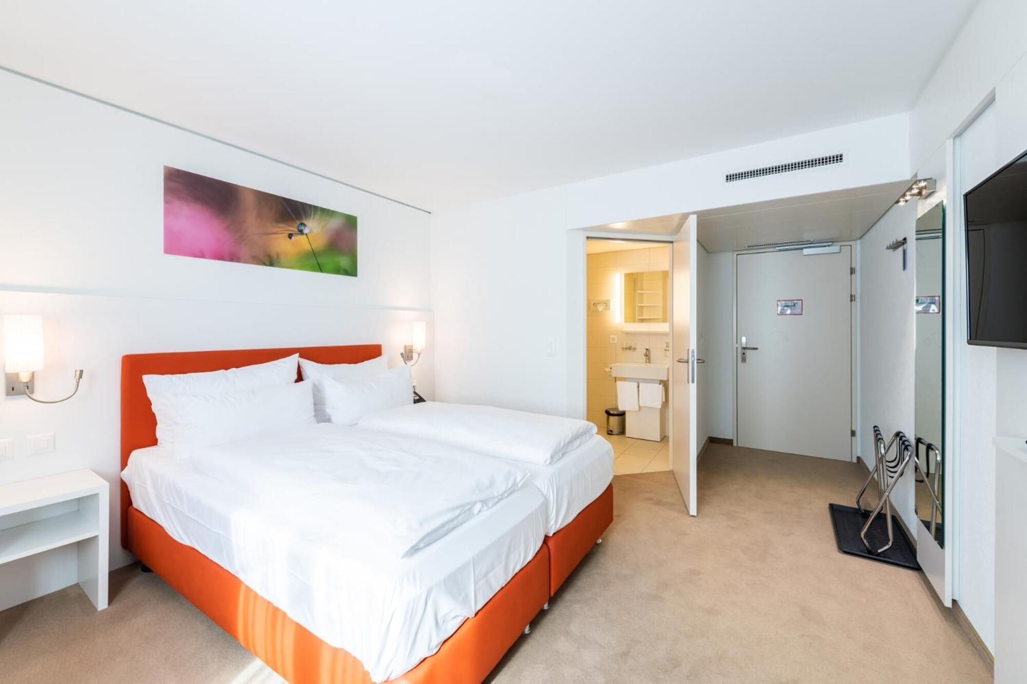 Ett hotellrum med en säng, sängbord, en tv och ett badrum som syns genom en öppen dörr.