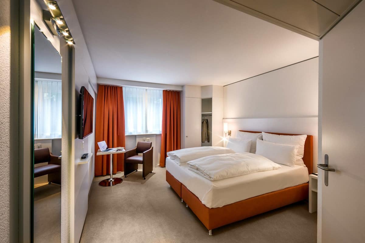 A hotel room with a bed, a desk with a laptop, a chair, and a wardrobe.
