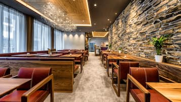 Un restaurant avec des tables en bois, des banquettes en cuir rouge, des murs en pierre et un lustre.