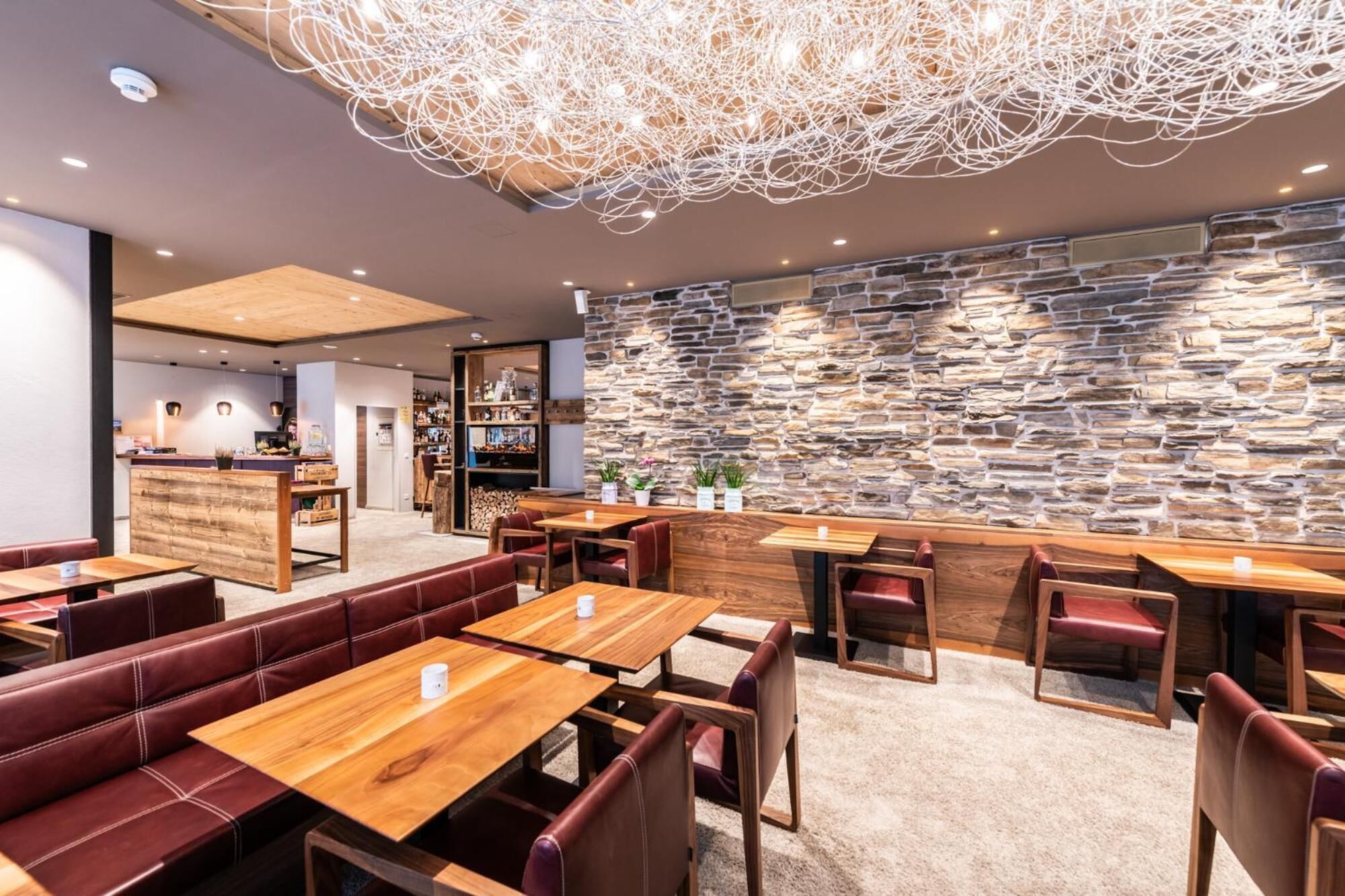 Interior moderno de restaurante con mesas de madera, asientos tapizados en cuero, pared de piedra y una lámpara de techo original.