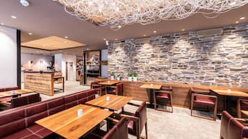 A modern restaurant interior with wooden tables and leather booths, a stone wall, and a unique ceiling light fixture.