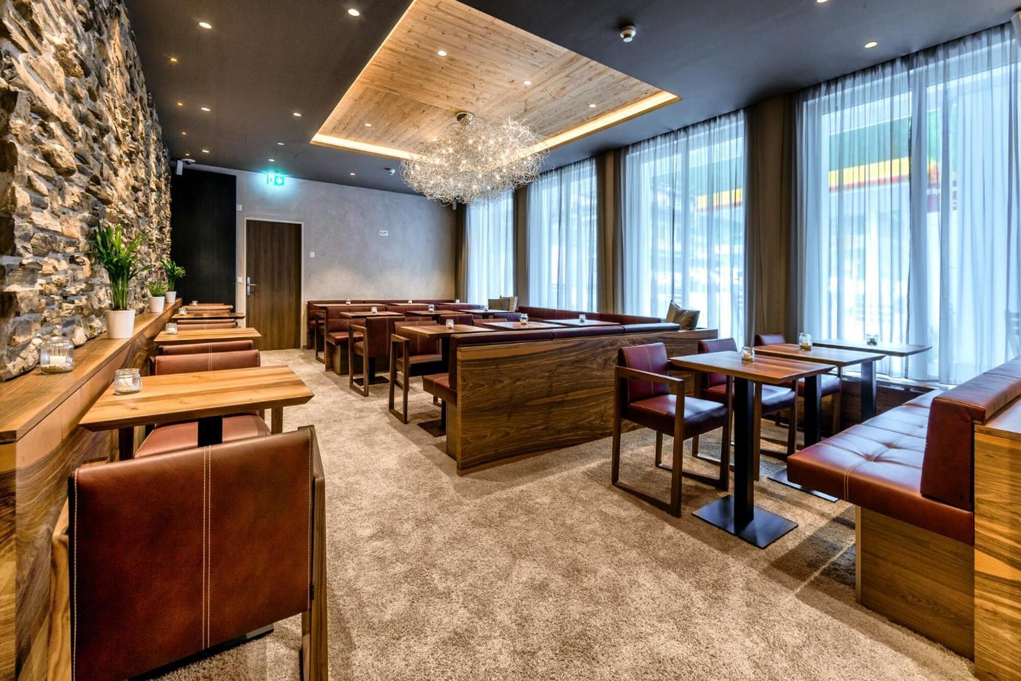 A modern restaurant with wooden tables and leather booths, stone walls, and large windows.