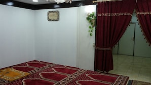 Une pièce dotée d’un tapis à motifs, d’un lustre, d’un tapis de prière et d’une plaque commémorative accrochée au mur.