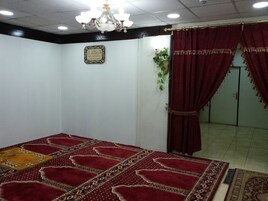 Una habitación con alfombra estampada, candelabro, un tapete de oración y una placa con motivos religiosos en la pared.