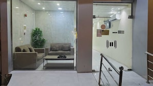 Un hall d’hôtel comprenant un comptoir d’accueil, un espace détente avec un canapé et des fauteuils, et un escalier menant aux étages supérieurs.
