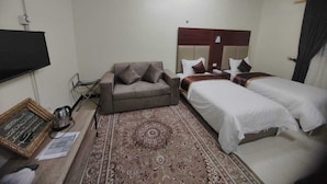 Une chambre d’hôtel avec un canapé, deux lits simples, une grande moquette et un téléviseur à écran plat.
