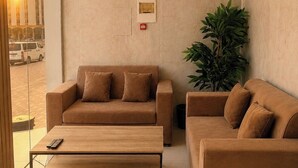A modern lobby with a beige sofa set, a wooden coffee table, and a large potted plant.