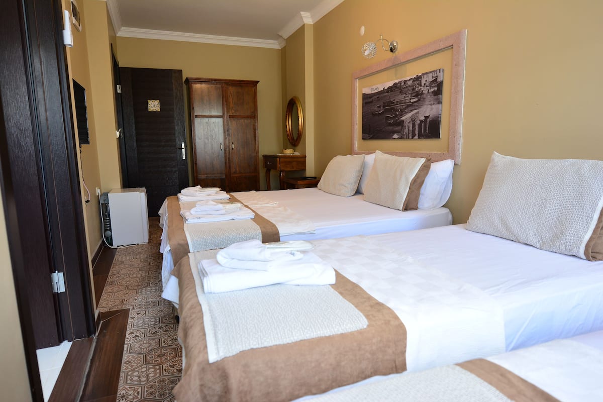 A hotel room with two beds, a wooden wardrobe, a framed picture on the wall, and a door with a number sign.