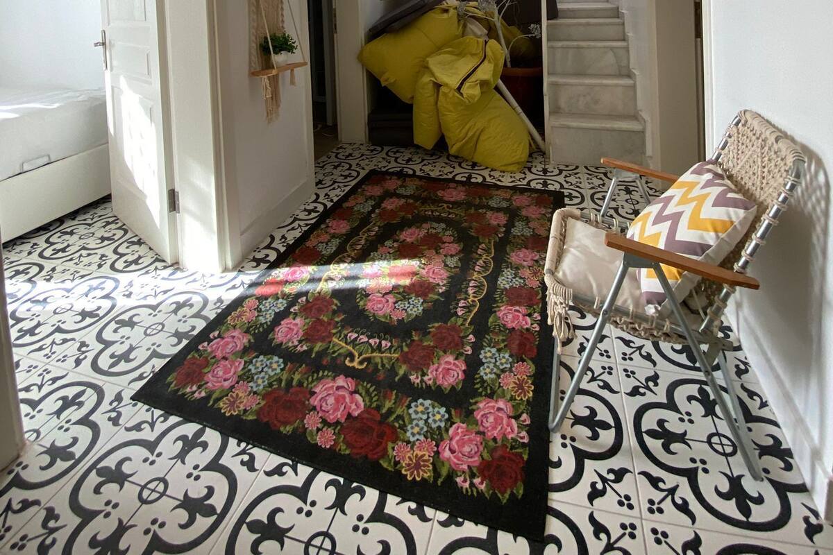 A hallway with a patterned floor, a chandelier, a staircase, and a chair with cushions.