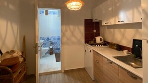 Een kleine keuken met houten kastjes, een wit aanrechtblad en een hangende lamp.