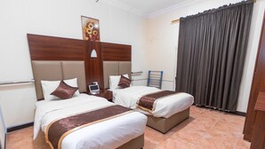 Een hotelkamer met twee bedden, een houten hoofdeinde, een bureau met een laptop en een groot raam met gordijnen.
