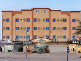 Un edificio de varios pisos con entrada central, unidades de aire acondicionado y varias tiendas a nivel de calle.