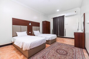 Habitación de hotel con dos camas, cabecera de madera, un ventanal con cortinas, equipo de aire acondicionado y un escritorio pequeño con espejo.