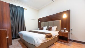 Une chambre d’hôtel avec un grand lit, une table de chevet avec un téléphone et une petite table de nuit avec une lampe.